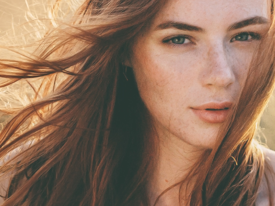 Ragazza con capelli castani tendenti al rosso che sorride. Lei in mezzo alla natura